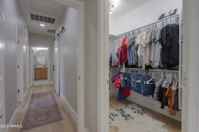 walk in closet with a barn door, visible vents, and wood finished floors