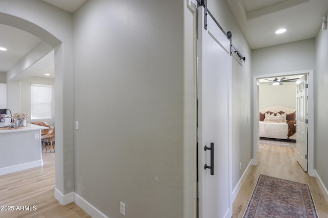 hall with light wood finished floors, a barn door, arched walkways, baseboards, and recessed lighting