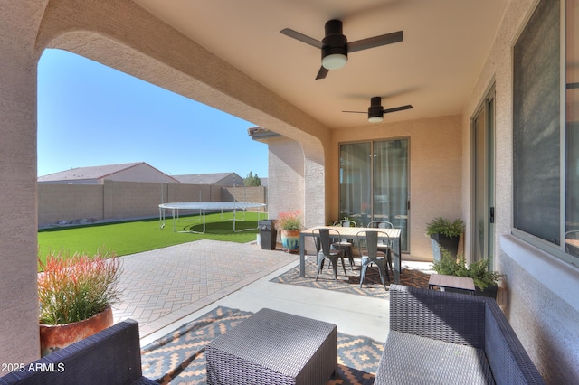 view of patio with ceiling fan, outdoor dining space, a trampoline, and fence