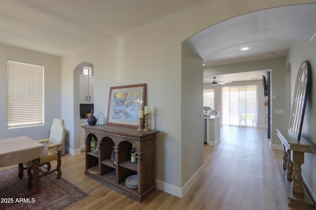 corridor with light wood-style floors, arched walkways, and baseboards