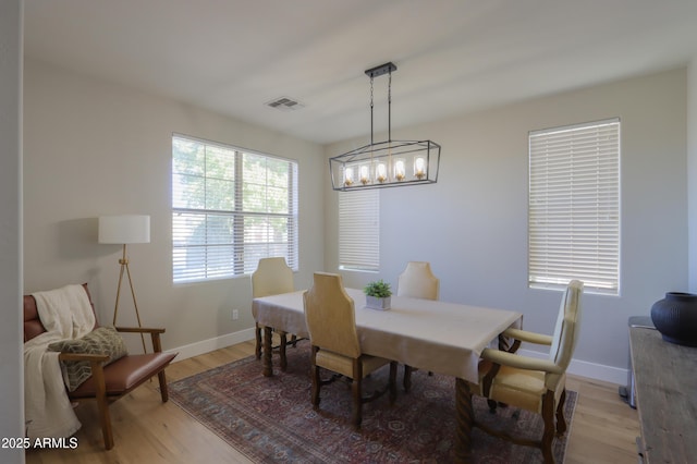 dining area featuring light wood-type flooring, an inviting chandelier, baseboards, and visible vents