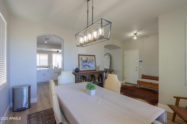 dining space with arched walkways, baseboards, and light wood finished floors