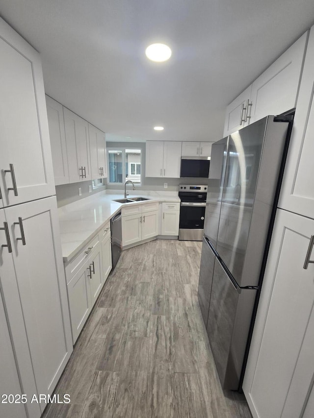 kitchen with appliances with stainless steel finishes, white cabinets, a sink, and light countertops