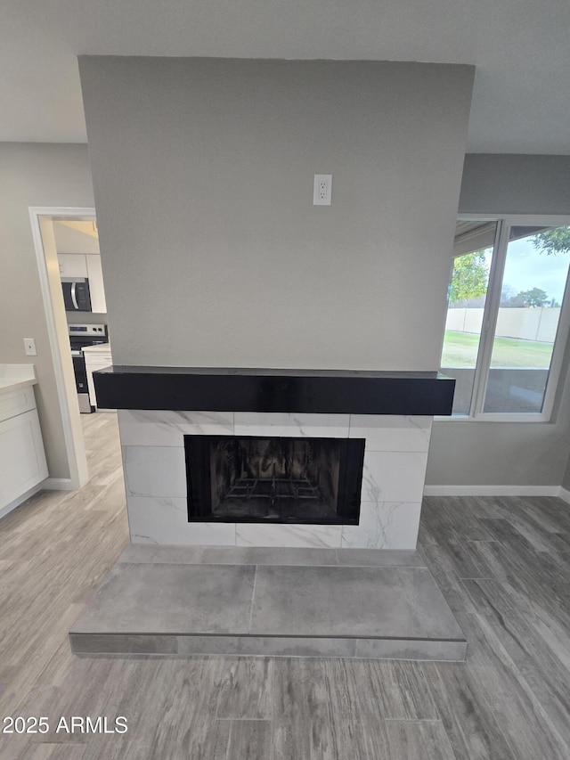 room details with a tiled fireplace, baseboards, stainless steel appliances, and wood finished floors