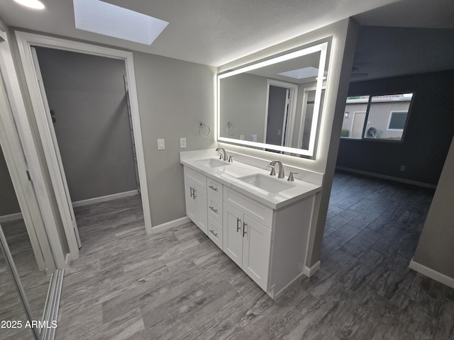 full bathroom featuring a skylight, a sink, baseboards, and wood finished floors