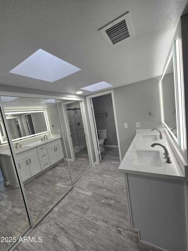 bathroom featuring a skylight, a sink, visible vents, and a shower stall