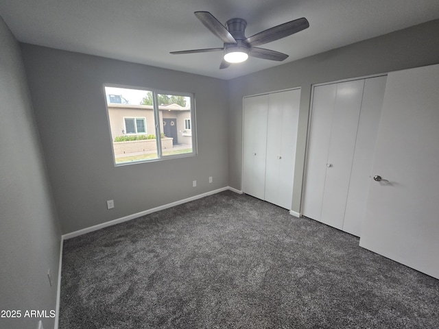 unfurnished bedroom with baseboards, dark carpet, a ceiling fan, and multiple closets