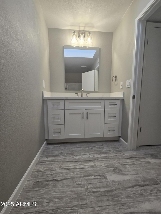 bathroom with a textured wall, vanity, a textured ceiling, wood finished floors, and baseboards