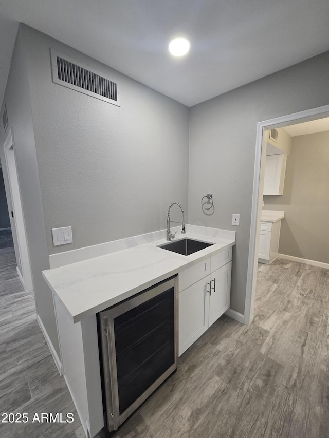 bar with beverage cooler, wood finished floors, a sink, visible vents, and baseboards