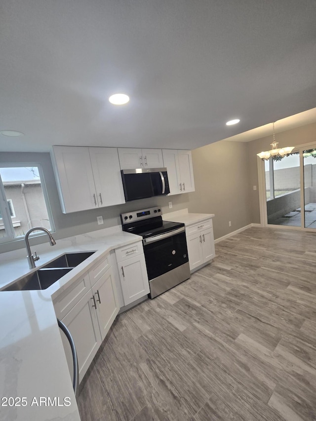 kitchen featuring a notable chandelier, stainless steel appliances, light wood-style floors, white cabinets, and a sink