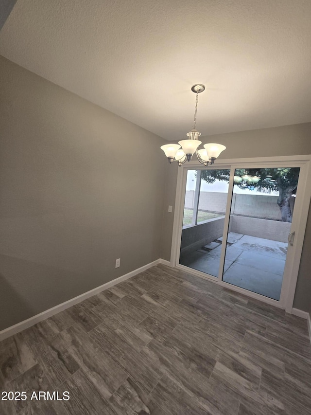 unfurnished dining area with dark wood-style flooring, a notable chandelier, and baseboards