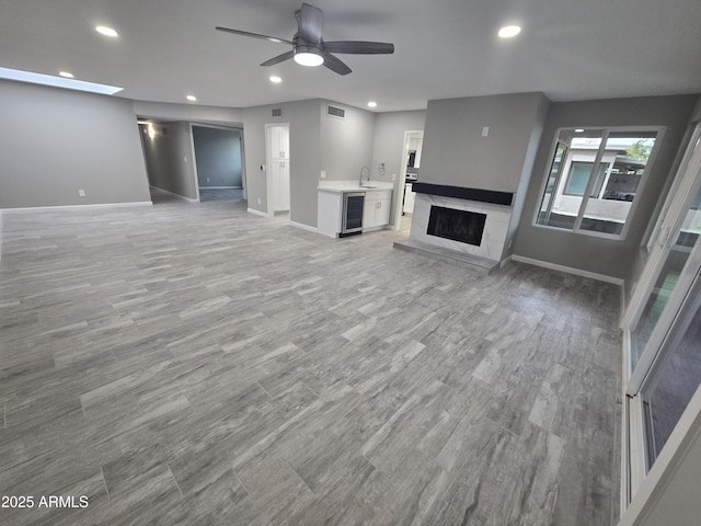 unfurnished living room featuring light wood-style flooring, recessed lighting, beverage cooler, a ceiling fan, and baseboards