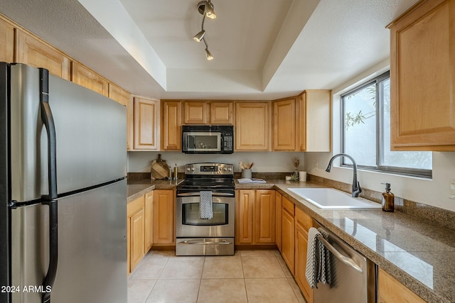 kitchen with stainless steel appliances, a tray ceiling, sink, light tile patterned floors, and light brown cabinets