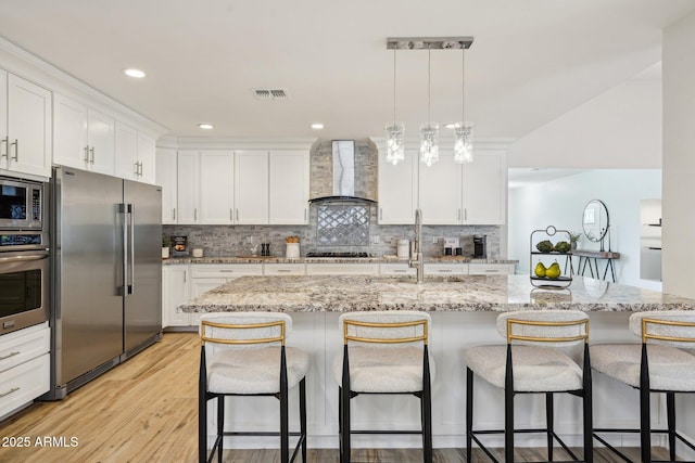 4920 E Osborn Rd, Phoenix, AZ 85018 - kitchen featuring appliances with stainless steel finishes, wall chimney exhaust hood, a sink, a breakfast bar, and white cabinetry