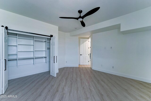 3903 E Melody Dr, Phoenix, AZ 85042 - unfurnished bedroom with a barn door, baseboards, wood finished floors, and a ceiling fan