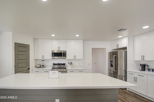 kitchen featuring a kitchen island, appliances with stainless steel finishes, white cabinets, dark hardwood / wood-style flooring, and light stone counters