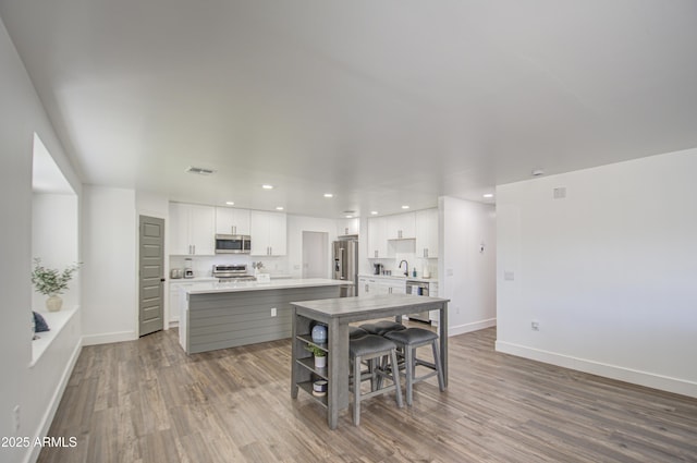 kitchen with stainless steel appliances, a center island, wood-type flooring, and white cabinets