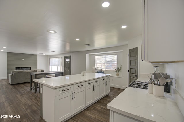 kitchen with a kitchen island, dark hardwood / wood-style floors, a fireplace, white cabinetry, and light stone counters