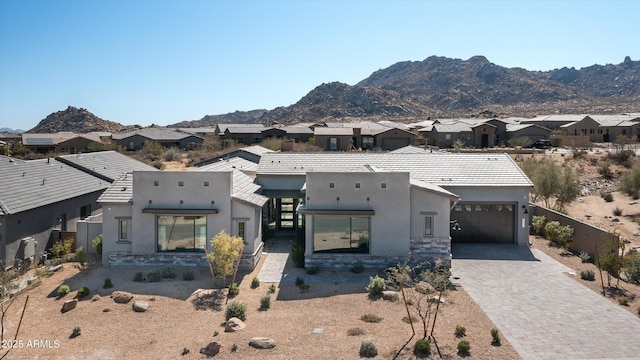 view of front of house with a garage, fence, decorative driveway, a mountain view, and stucco siding