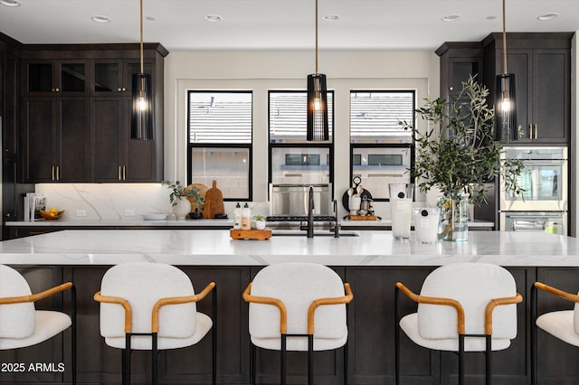 kitchen featuring light stone counters, pendant lighting, tasteful backsplash, double oven, and a sink