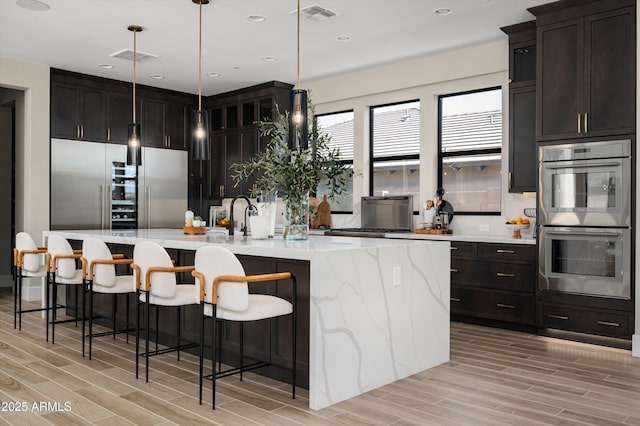 kitchen with light stone counters, stainless steel double oven, visible vents, a large island, and wood tiled floor