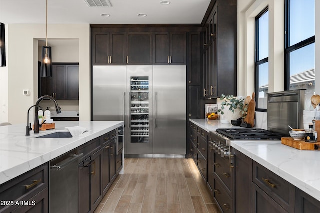 kitchen featuring stainless steel appliances, hanging light fixtures, light wood-style flooring, a sink, and light stone countertops