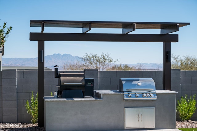 view of patio with an outdoor kitchen, grilling area, fence, and a mountain view