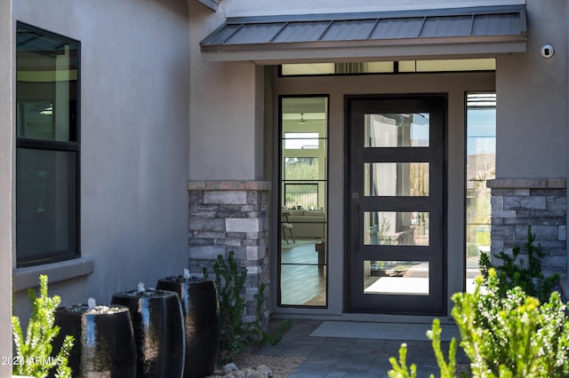 doorway to property with metal roof, stone siding, a standing seam roof, and stucco siding