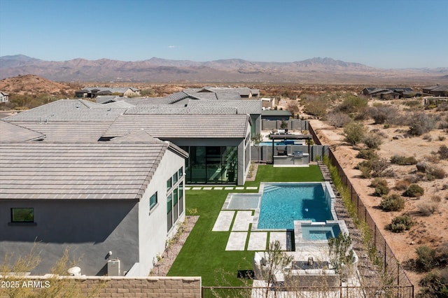 view of swimming pool featuring a pool with connected hot tub, a fenced backyard, a lawn, and a mountain view