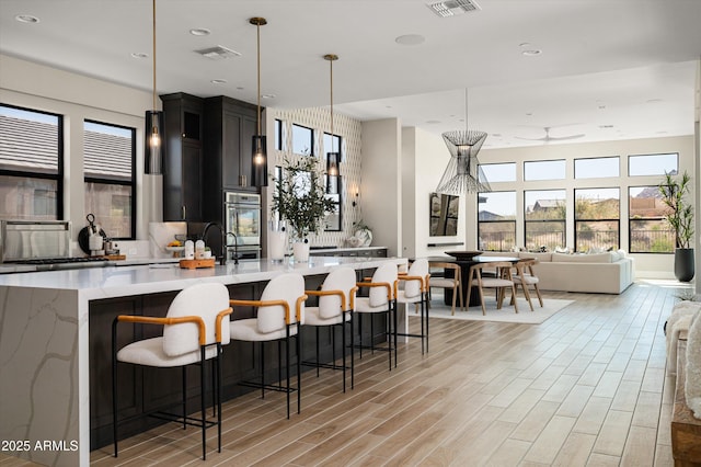 kitchen with visible vents, a spacious island, open floor plan, dark cabinetry, and light wood-style floors