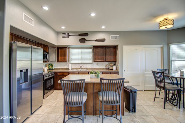 kitchen featuring dark brown cabinets, appliances with stainless steel finishes, a center island, and decorative backsplash