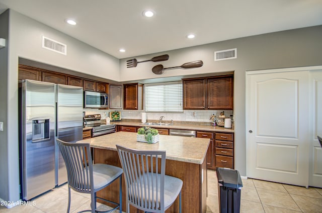 kitchen featuring decorative backsplash, light tile patterned floors, stainless steel appliances, sink, and a center island