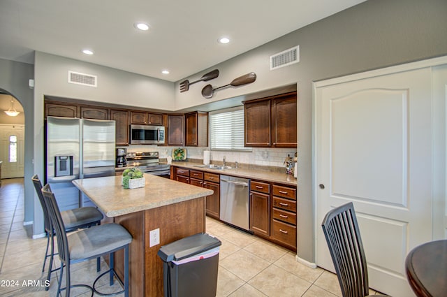 kitchen with tasteful backsplash, appliances with stainless steel finishes, sink, a kitchen island, and light tile patterned floors