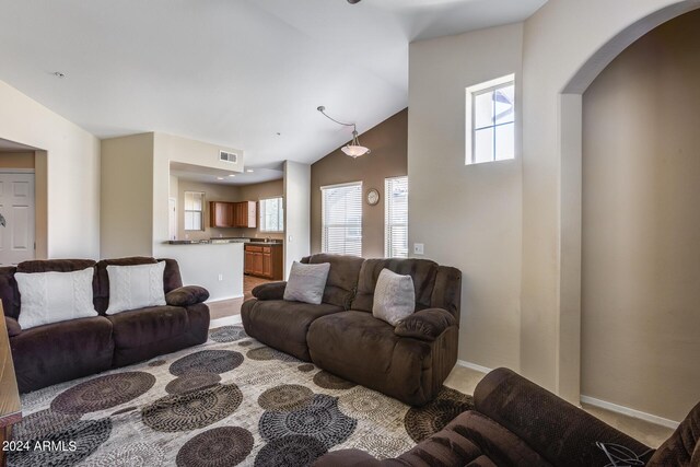 carpeted living room with baseboards, visible vents, arched walkways, high vaulted ceiling, and a sink