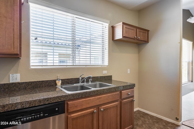 kitchen with dark tile patterned floors, stainless steel dishwasher, sink, and a wealth of natural light