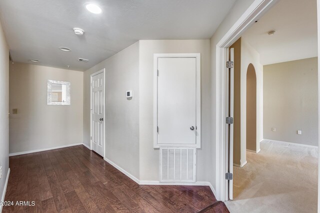 hall featuring arched walkways, wood finished floors, visible vents, and baseboards