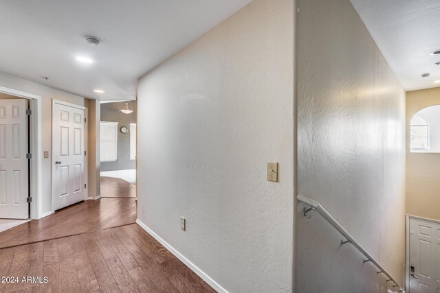 hallway with arched walkways, a textured wall, wood finished floors, an upstairs landing, and baseboards