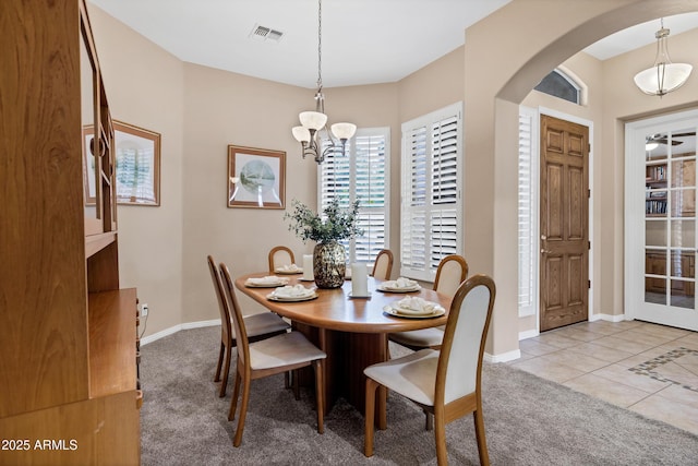 carpeted dining space featuring baseboards, visible vents, arched walkways, tile patterned flooring, and a notable chandelier