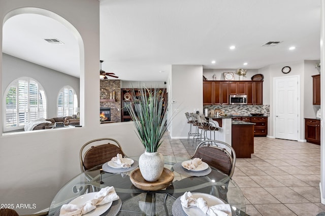 dining room featuring a stone fireplace, light tile patterned flooring, visible vents, and a ceiling fan