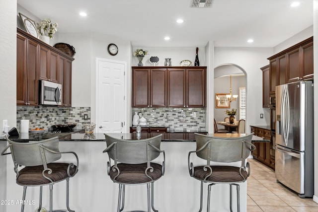 kitchen with arched walkways, appliances with stainless steel finishes, a breakfast bar area, a peninsula, and light tile patterned flooring