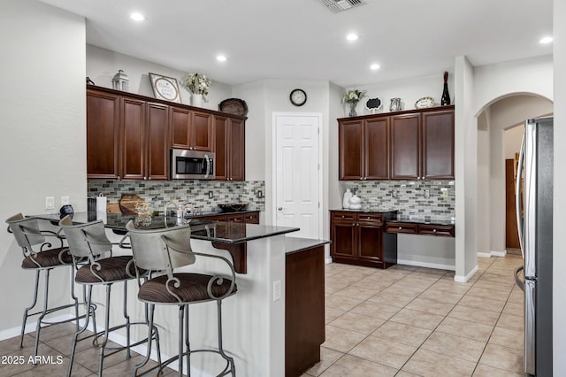 kitchen with arched walkways, light tile patterned flooring, a peninsula, a kitchen breakfast bar, and appliances with stainless steel finishes