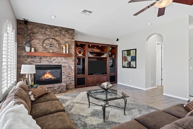 tiled living area with arched walkways, a fireplace, visible vents, ceiling fan, and baseboards