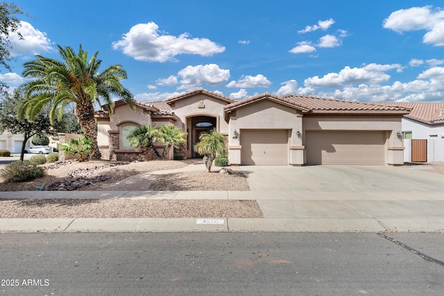 mediterranean / spanish-style home featuring a garage, driveway, a tiled roof, and stucco siding