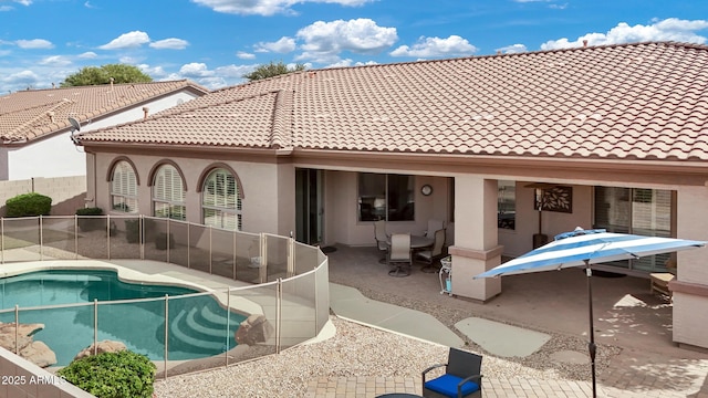 rear view of property with a patio, fence, a tiled roof, a fenced in pool, and stucco siding