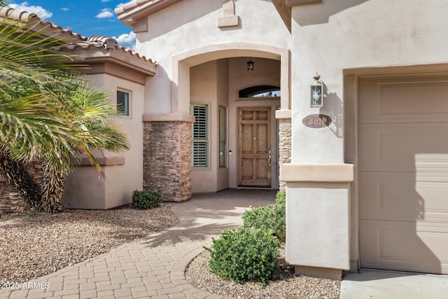 view of exterior entry featuring a garage, stone siding, a tile roof, and stucco siding