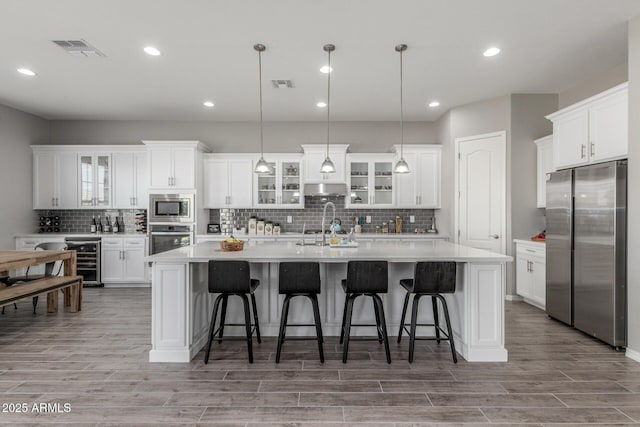 1342 E Milada Dr, Phoenix, AZ 85042 - kitchen with appliances with stainless steel finishes, a kitchen island with sink, backsplash, wine cooler, and light countertops