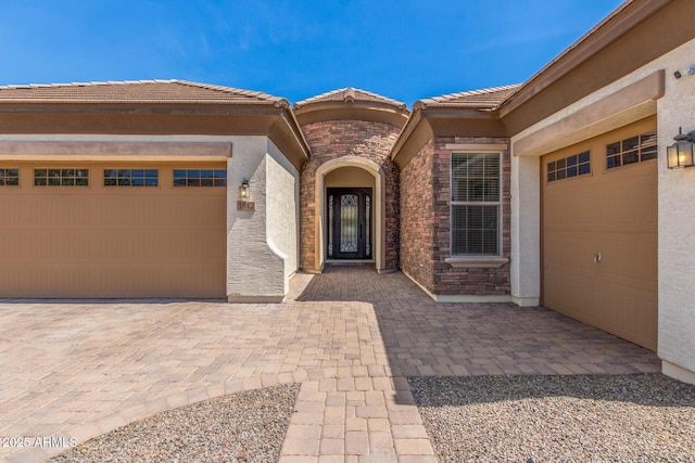 1342 E Milada Dr, Phoenix, AZ 85042 - view of exterior entry with an attached garage, a tile roof, decorative driveway, stucco siding, and stone siding