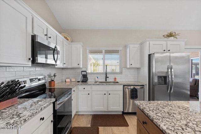 kitchen with tasteful backsplash, light stone counters, appliances with stainless steel finishes, white cabinets, and a sink