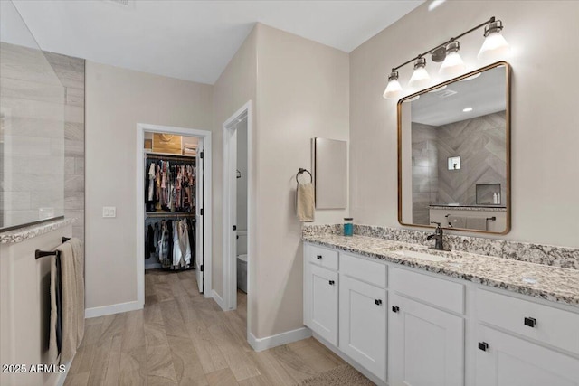 bathroom featuring baseboards, a spacious closet, vanity, and walk in shower