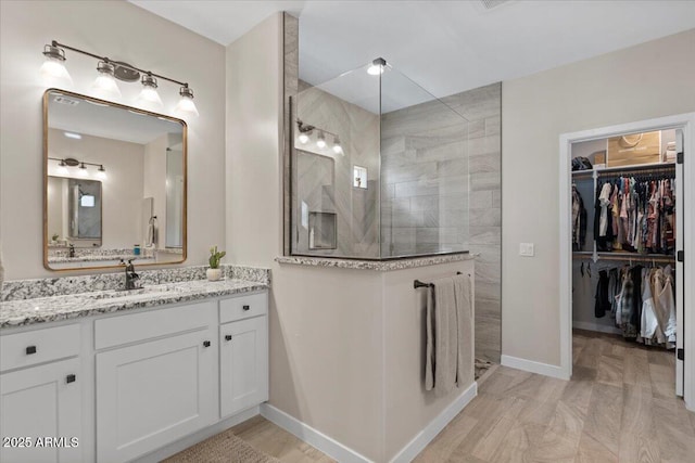 bathroom with vanity, a spacious closet, a walk in shower, and baseboards